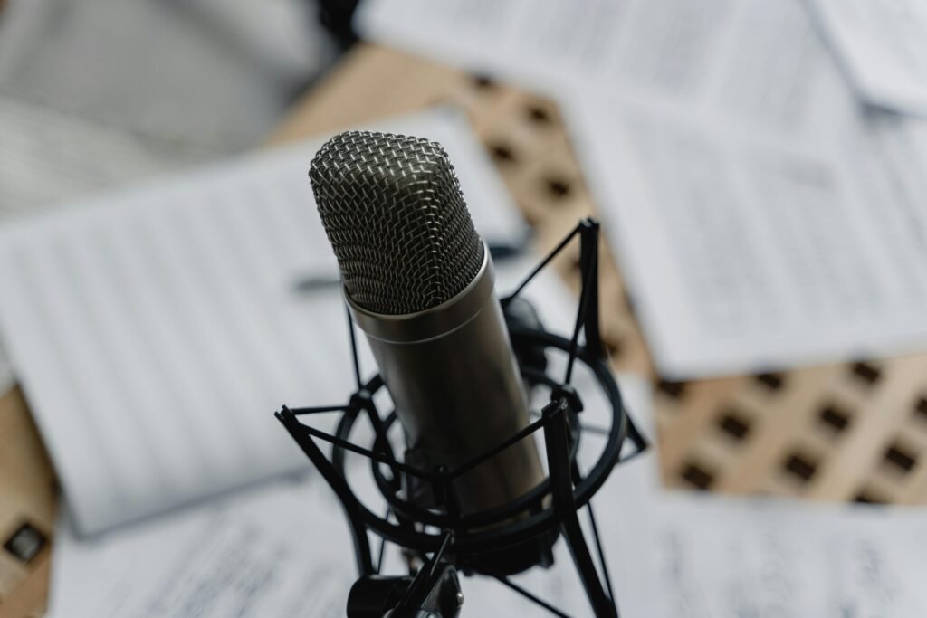 Close-up of a condenser microphone on a mic stand surrounded by music sheets in a studio setting.